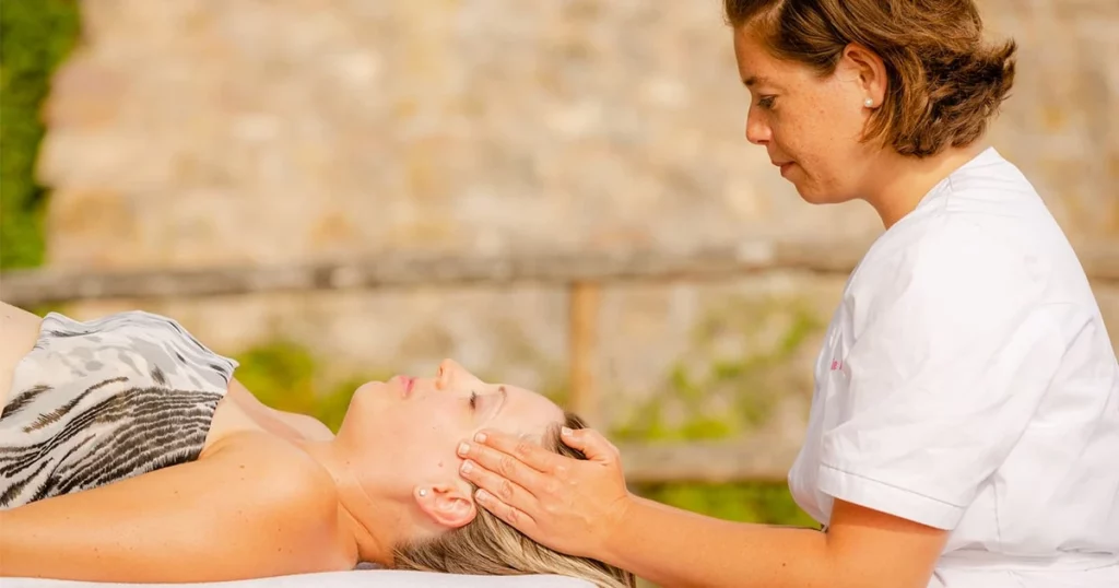 Femme allongée sur le dos sur une table de massage qui se fait masser les tempes par une esthéticienne